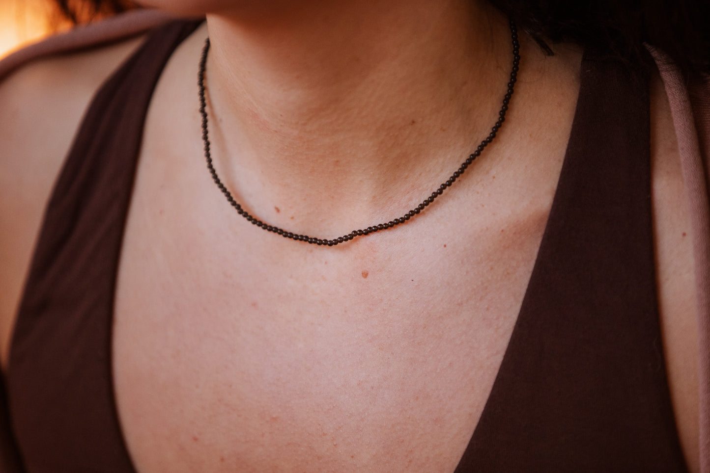 Close-up of a person wearing a dark obsidian beaded necklace with a blurred background
