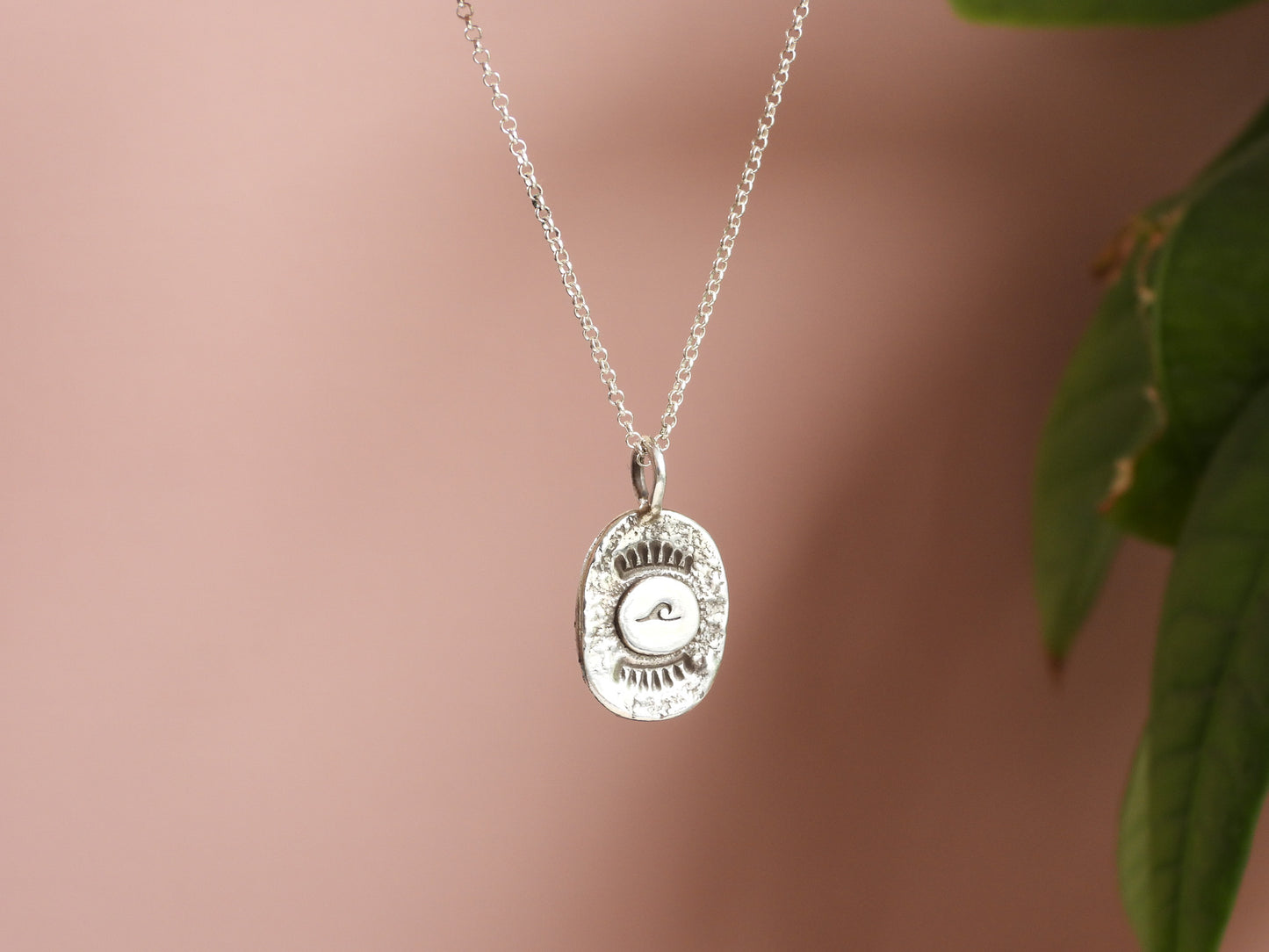Silver wave necklace with a round pendant on a soft pink background