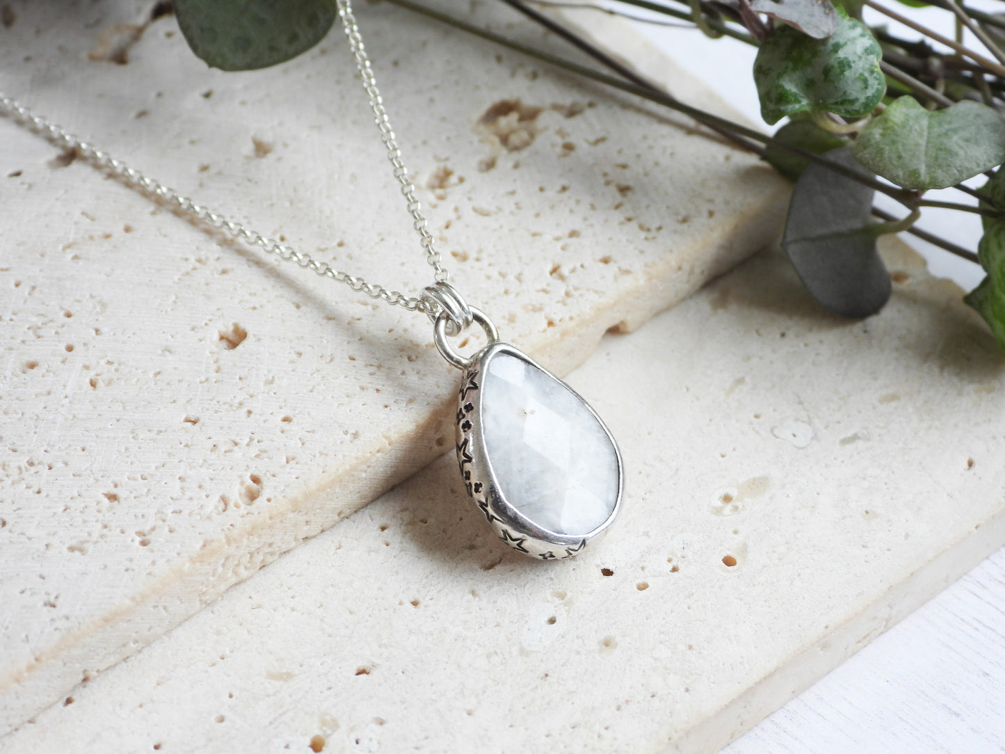 Teardrop-shaped silver moonstone pendant with a white stone on a light stone surface.