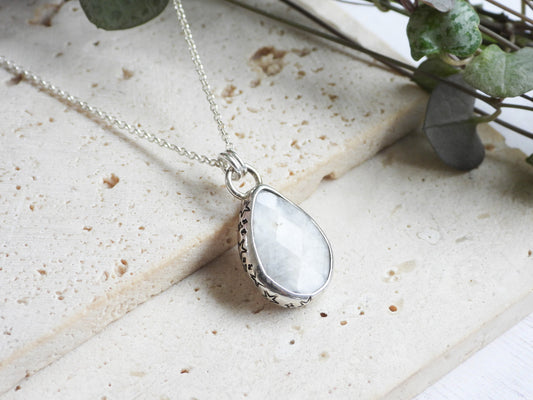 Teardrop-shaped silver moonstone pendant with a white stone on a light stone surface.