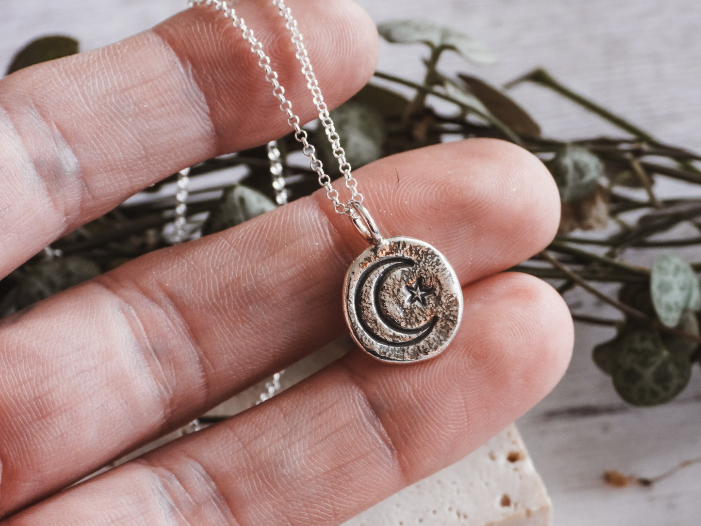 Hand holding a silver necklace with a moon and star pendant against a natural background