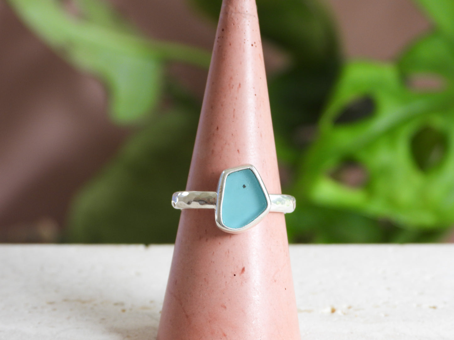Silver ring with a blue seaglass stone on a pink cone against a blurred green plant background