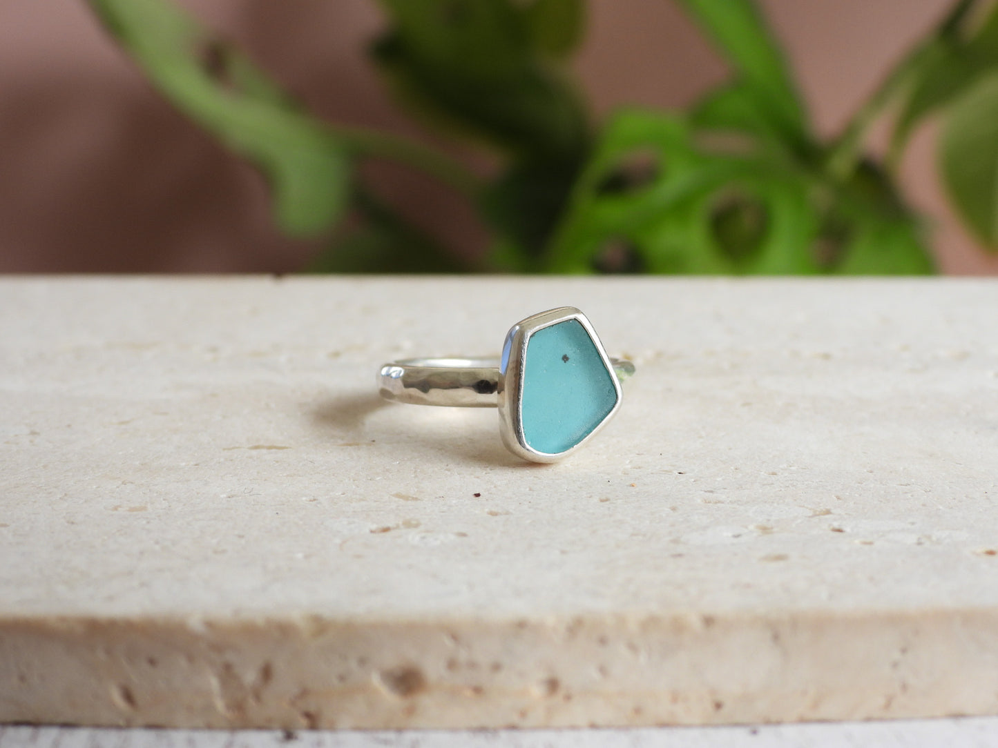 Silver ring with a turquoise stone on a wooden surface with a blurred plant background