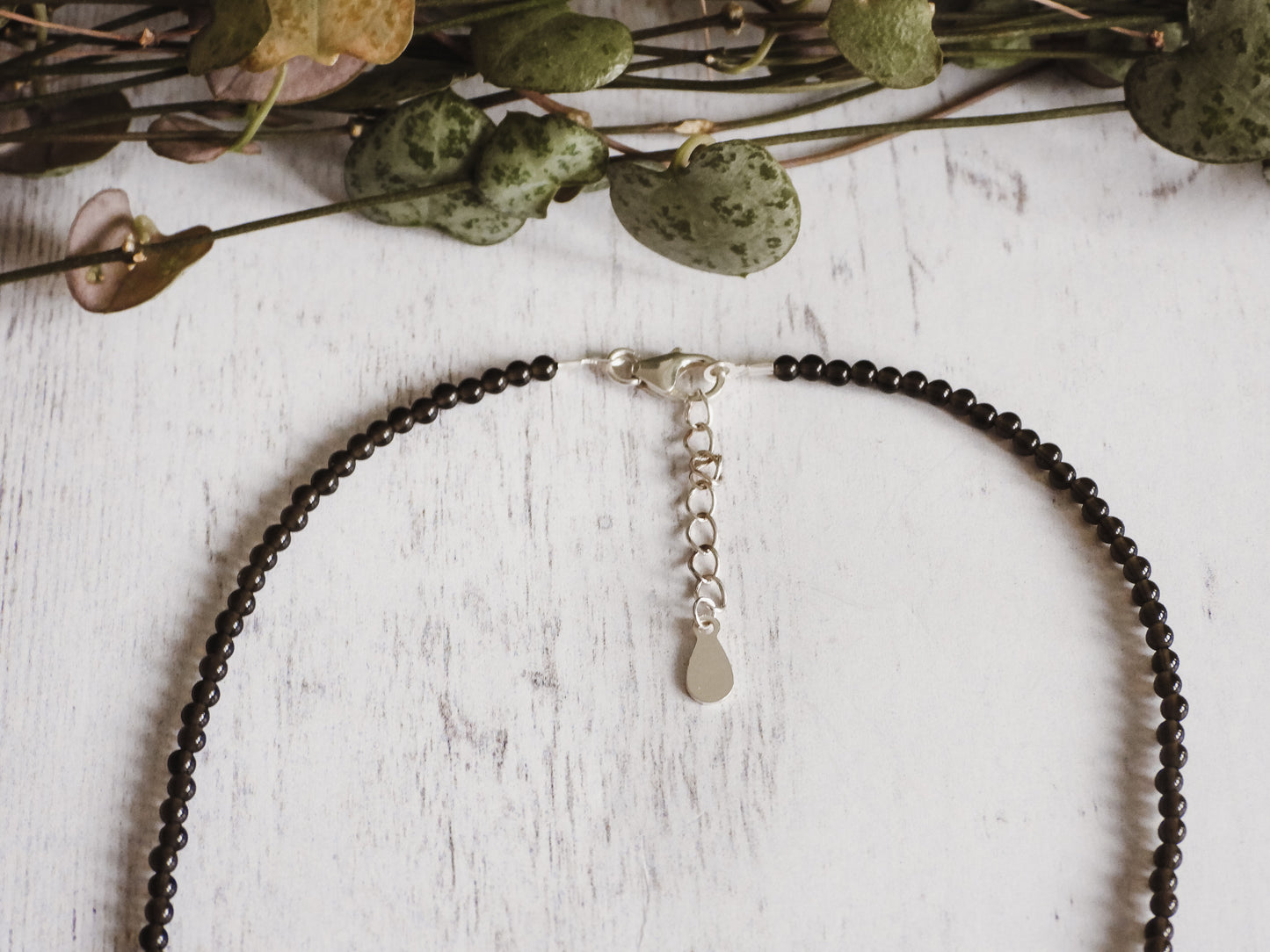 Beaded necklace with a solid silver clasp on a white wooden surface with greenery.