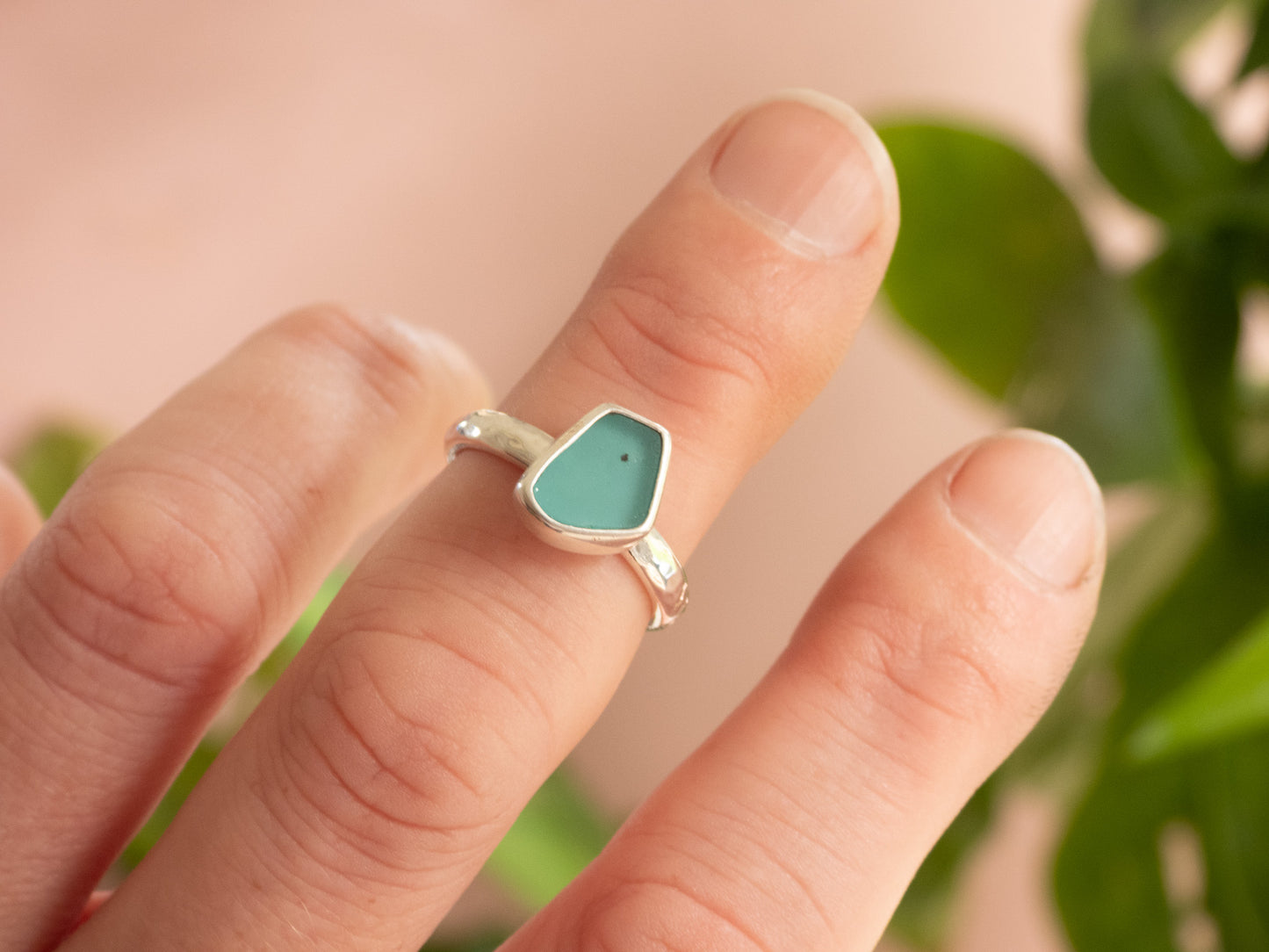 Hand wearing a silver ring with a turquoise seaglass stone against a blurred natural background