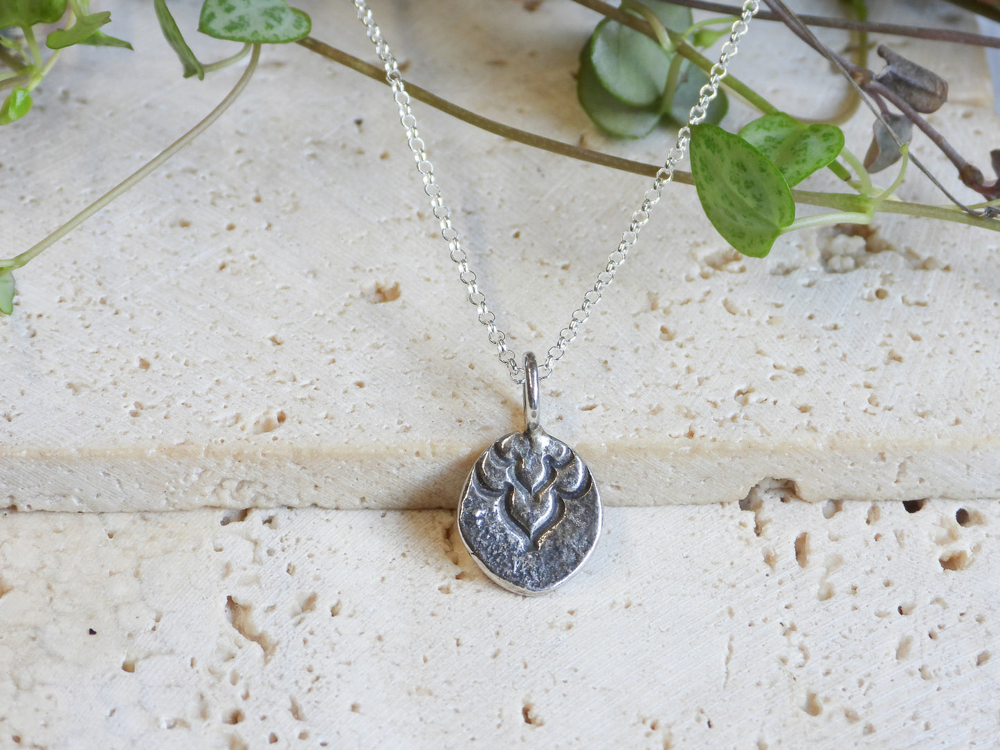 rustic Silver necklace with a pendant on a textured surface with green leaves in the background