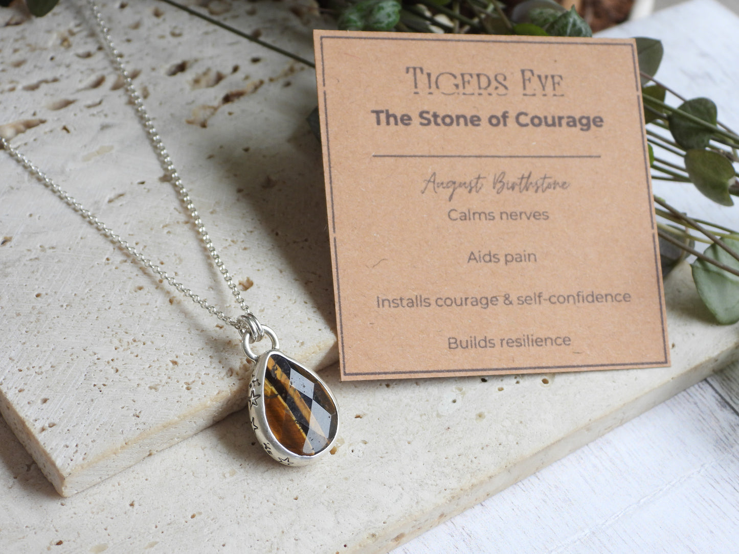 Tiger's Eye necklace with pendant on a stone surface next to a card describing its properties.