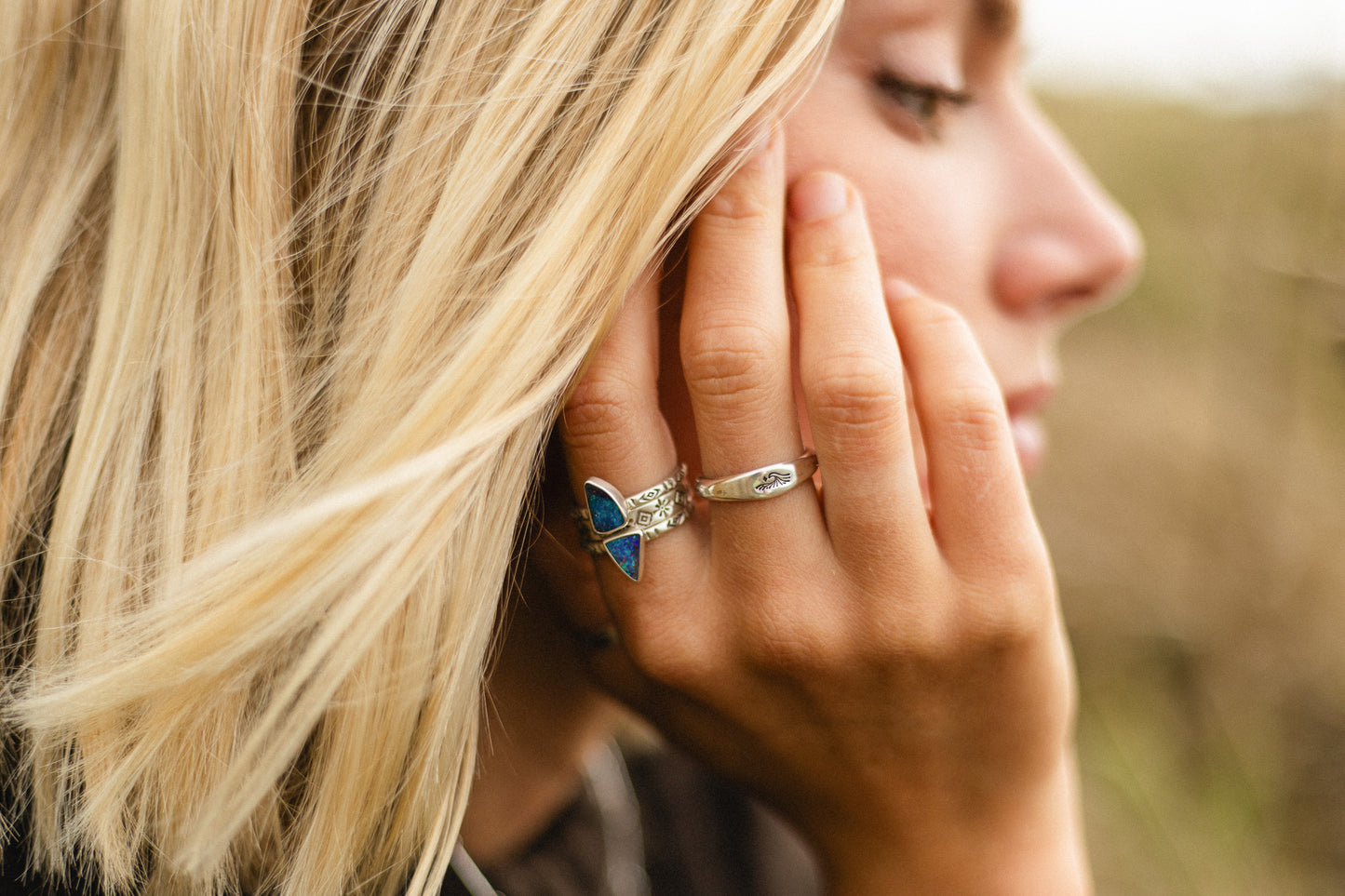 Close-up of a woman wearing a boulder opal stacking ring a blurred natural background