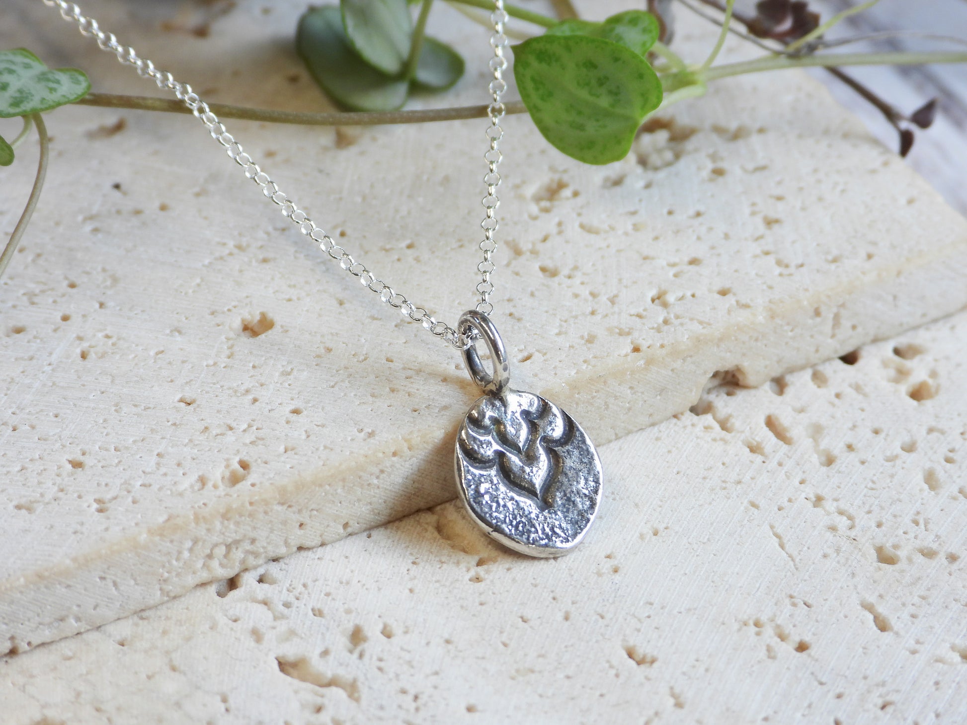 Silver boho necklace with a pendant on a light stone surface with green leaves in the background