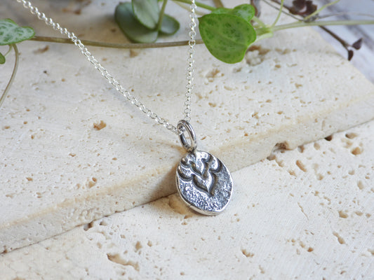 Silver boho necklace with a pendant on a light stone surface with green leaves in the background