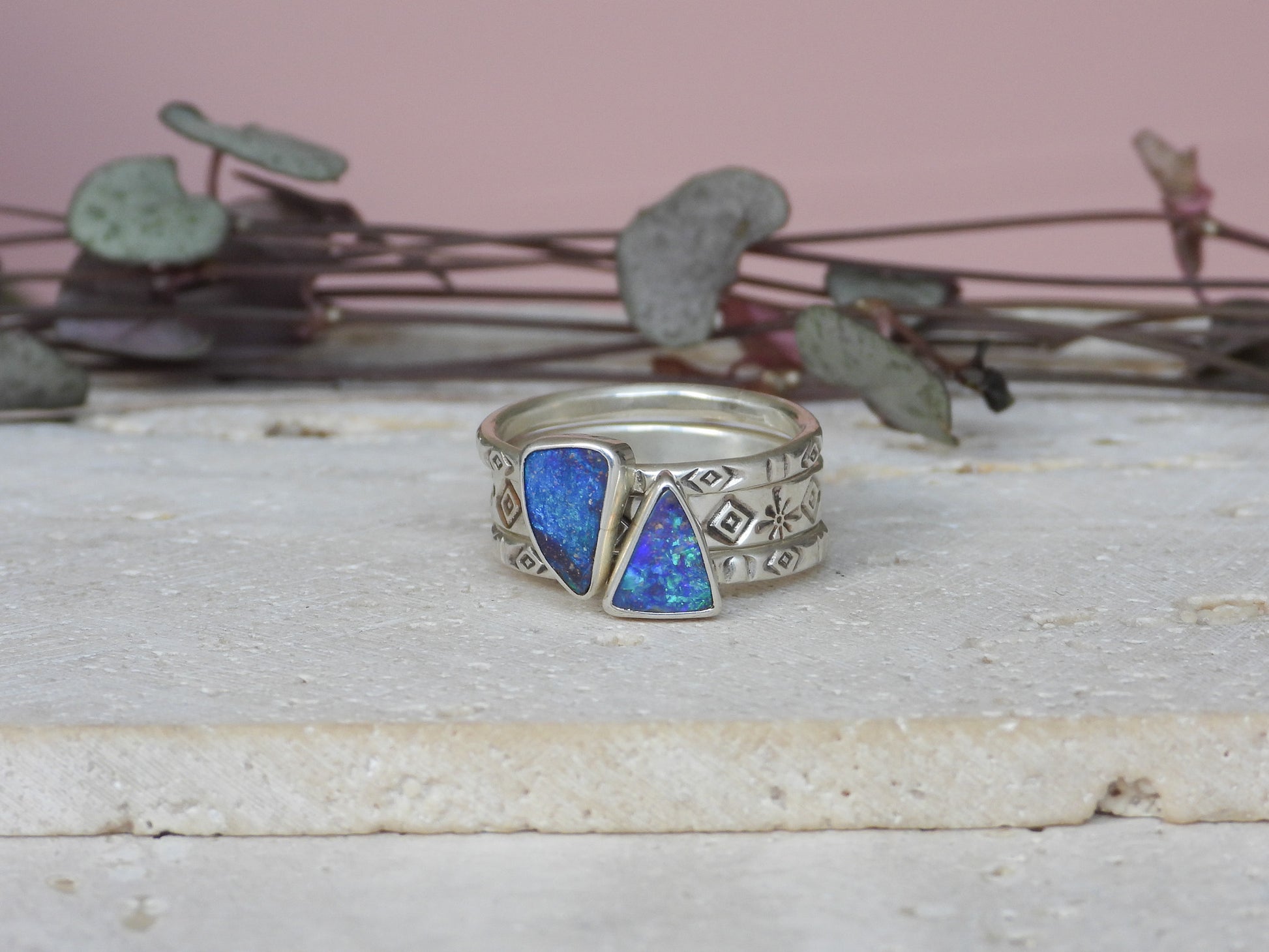 Silver ring with blue boulder opal gemstones on a wooden surface with plants in the background