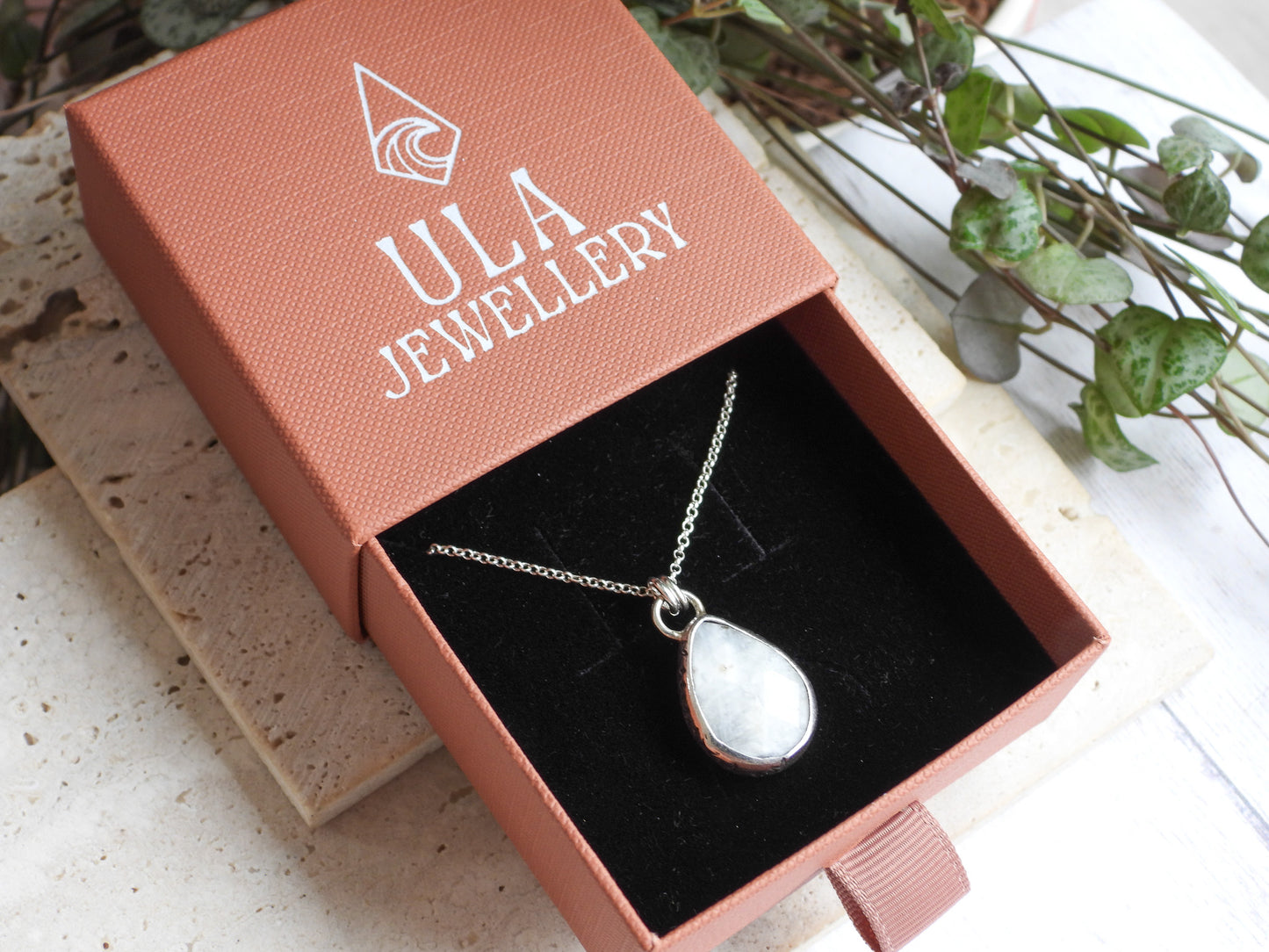 Teardrop-shaped pendant necklace in a ULA Jewellery box with a plant in the background