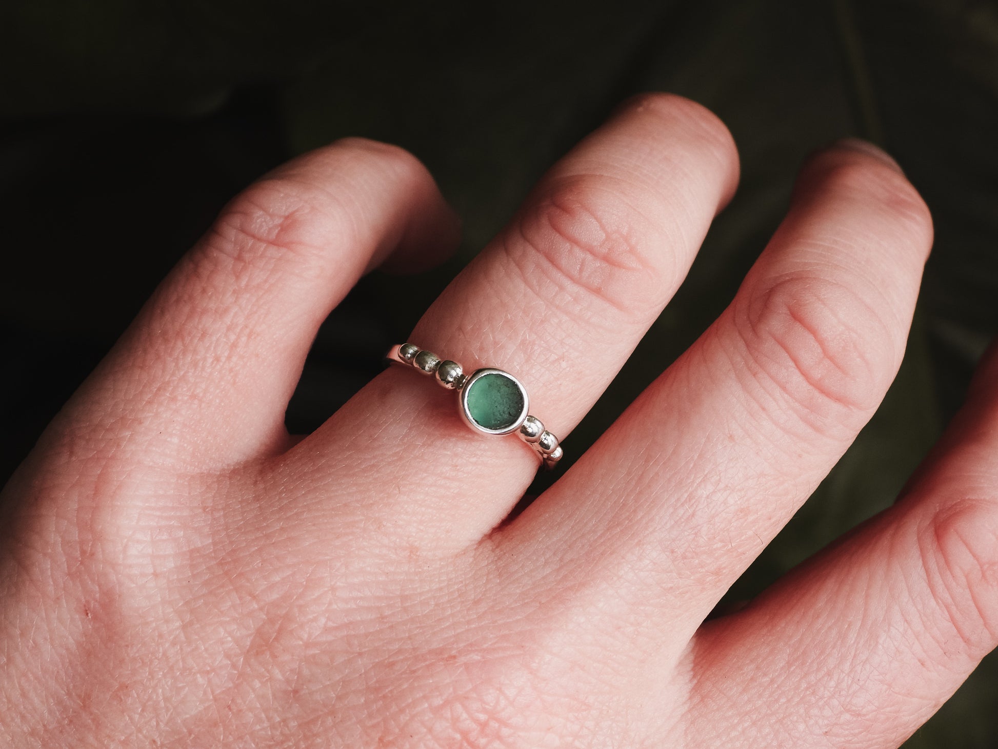 a hand wearing a teal green cornish seaglass ring