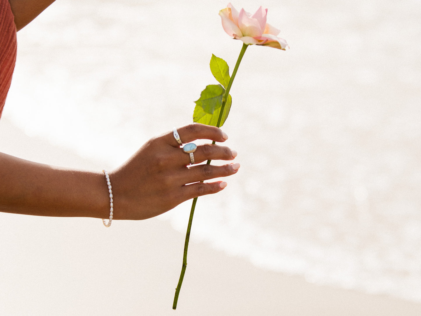 Hand holding a pink rose against a light background wearing bohemian jewellery