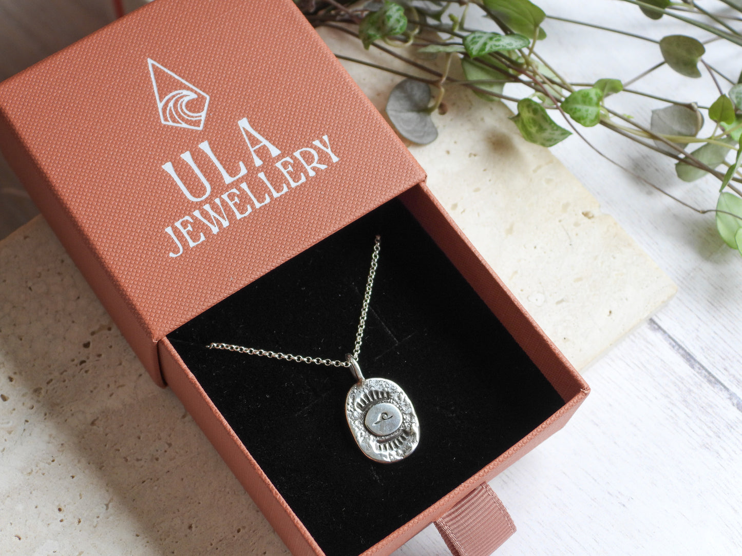 Silver wave necklace in a ULA Jewellery box on a light surface with greenery.