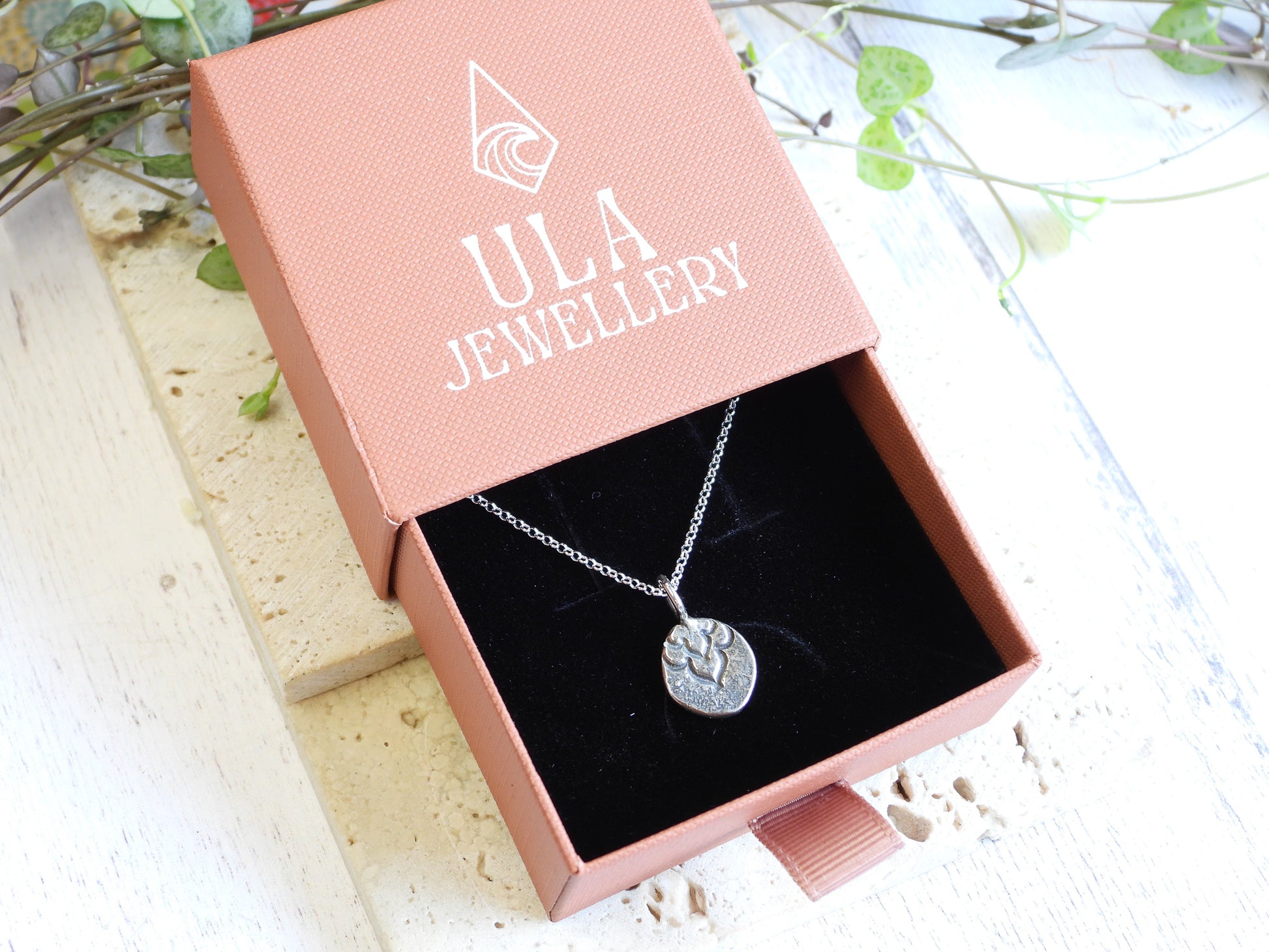 Silver necklace with a paw print pendant in a pink 'ULA Jewellery' box on a light wooden surface.