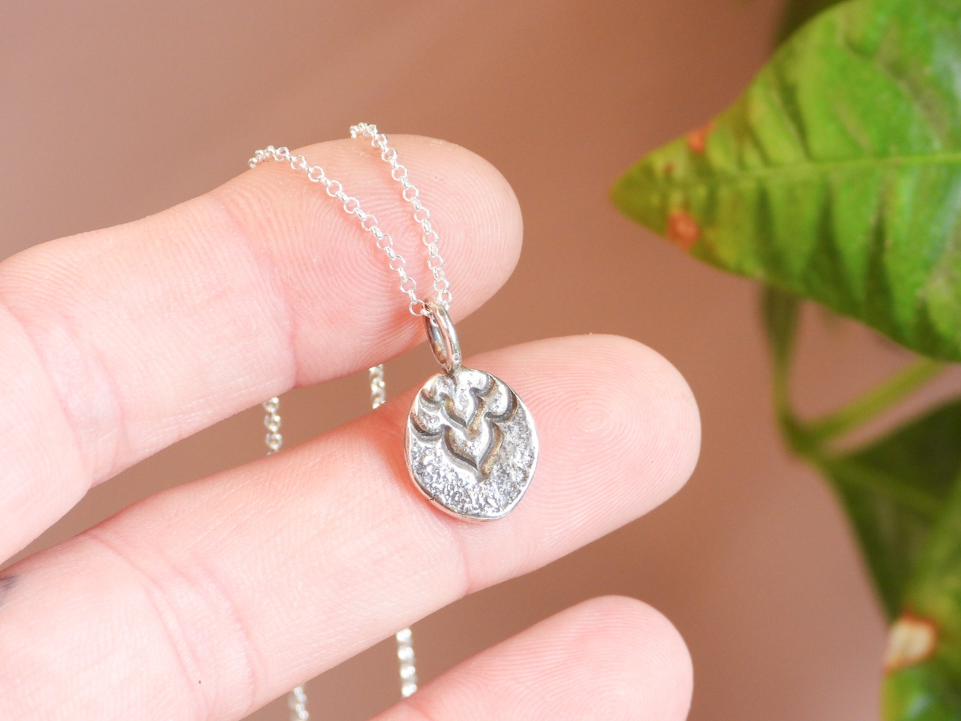 Silver necklace with a pendant held by a hand against a blurred natural background