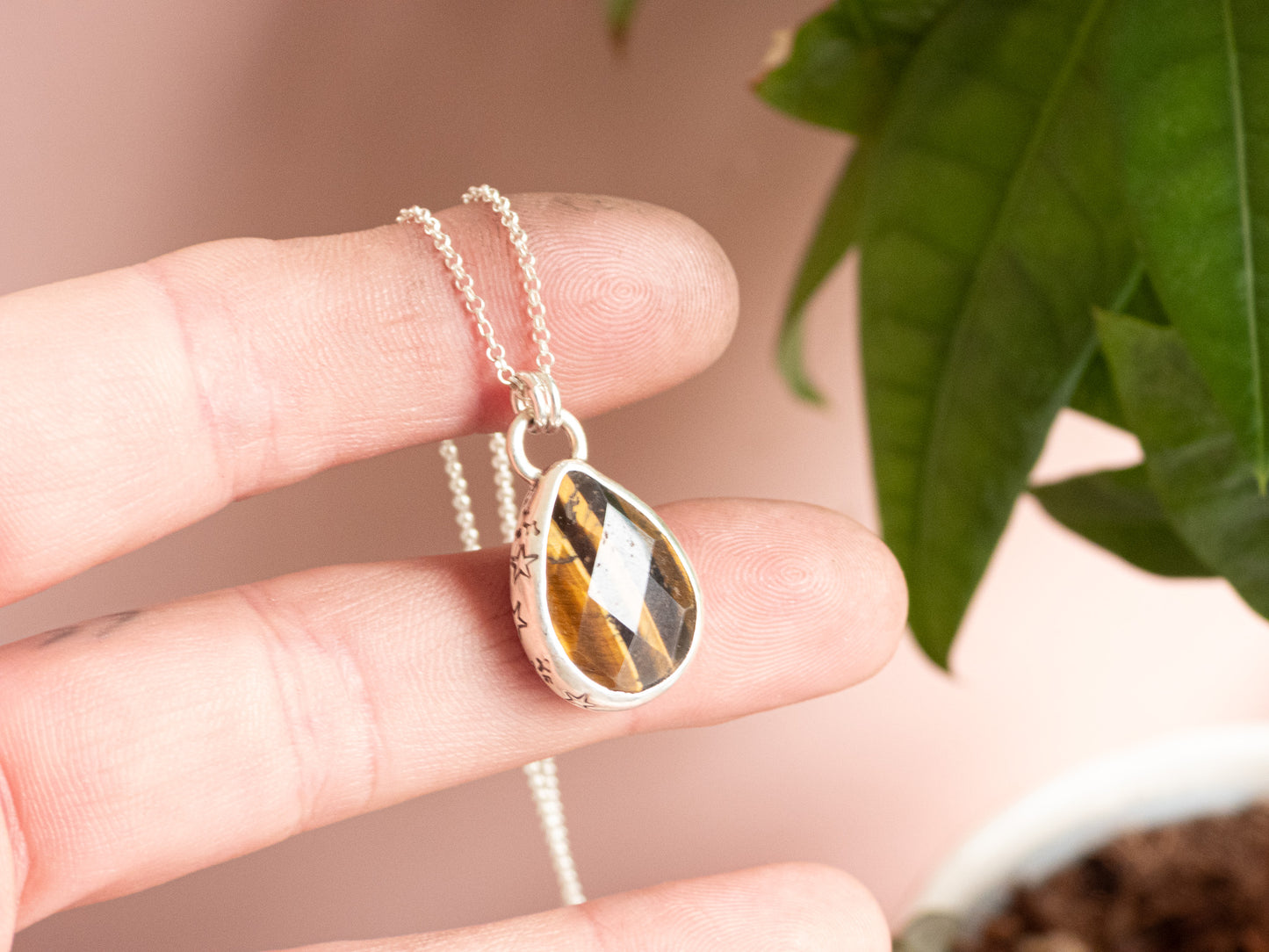 Teardrop-shaped pendant with tiger's eye pattern held between fingers against a blurred natural background