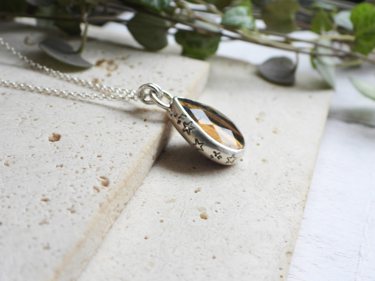 Silver tiger's eye pendant necklace on a textured surface with greenery in the background