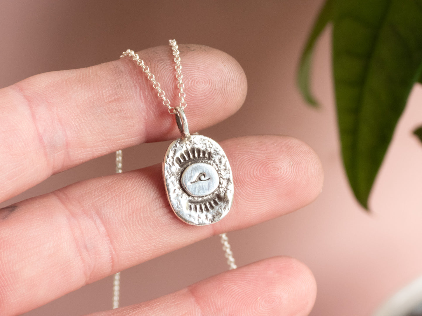 unique handmade silver wave charm necklace against a pink background