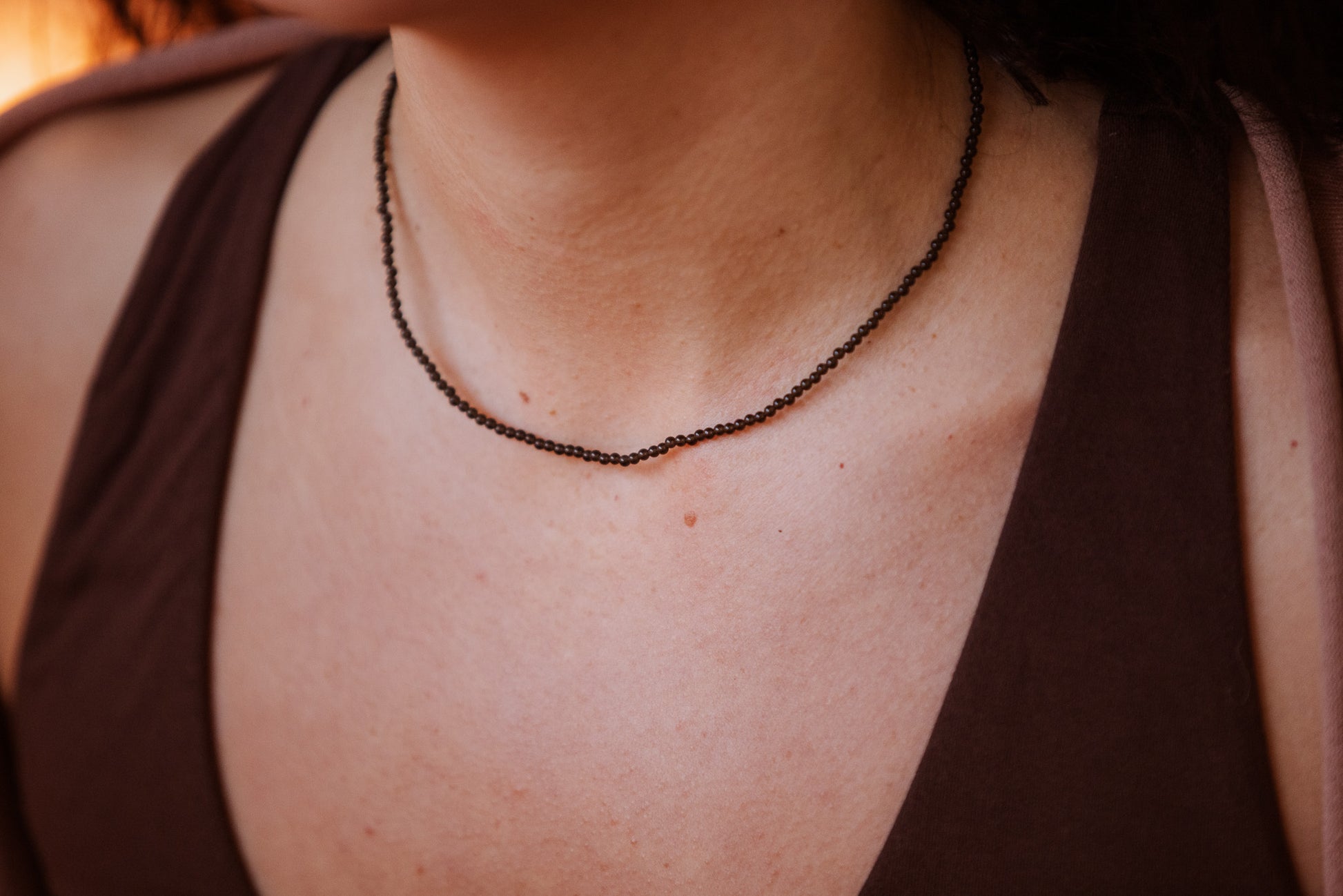 Close-up of a person wearing a dark obsidian beaded necklace with a blurred background