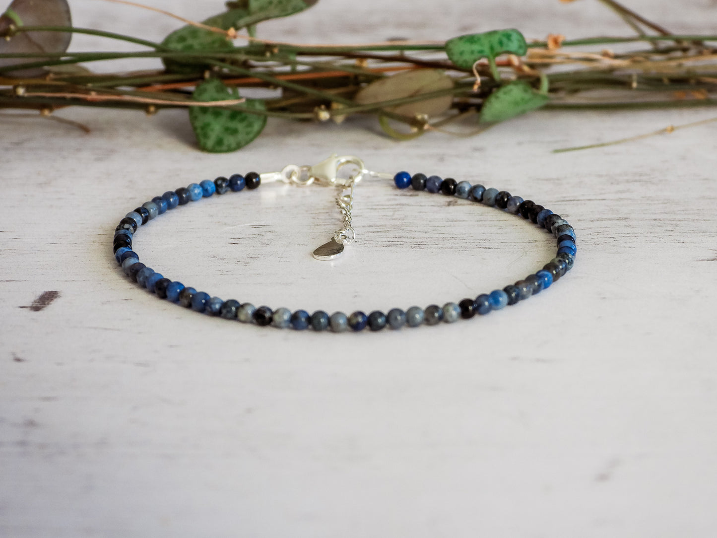 Blue sodalite beaded bracelet on a light wooden surface with green leaves in the background