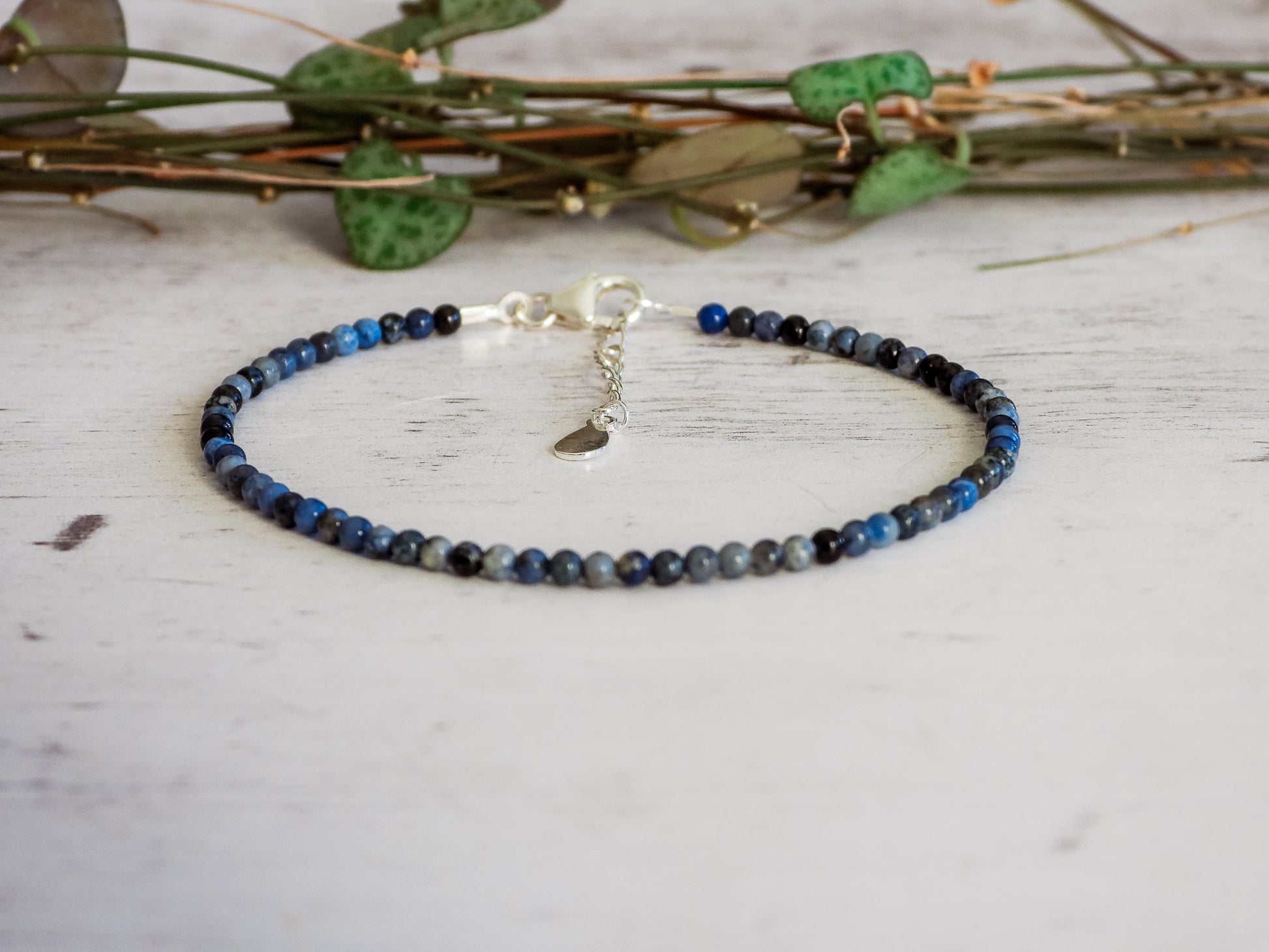 Blue sodalite beaded bracelet on a light wooden surface with green leaves in the background