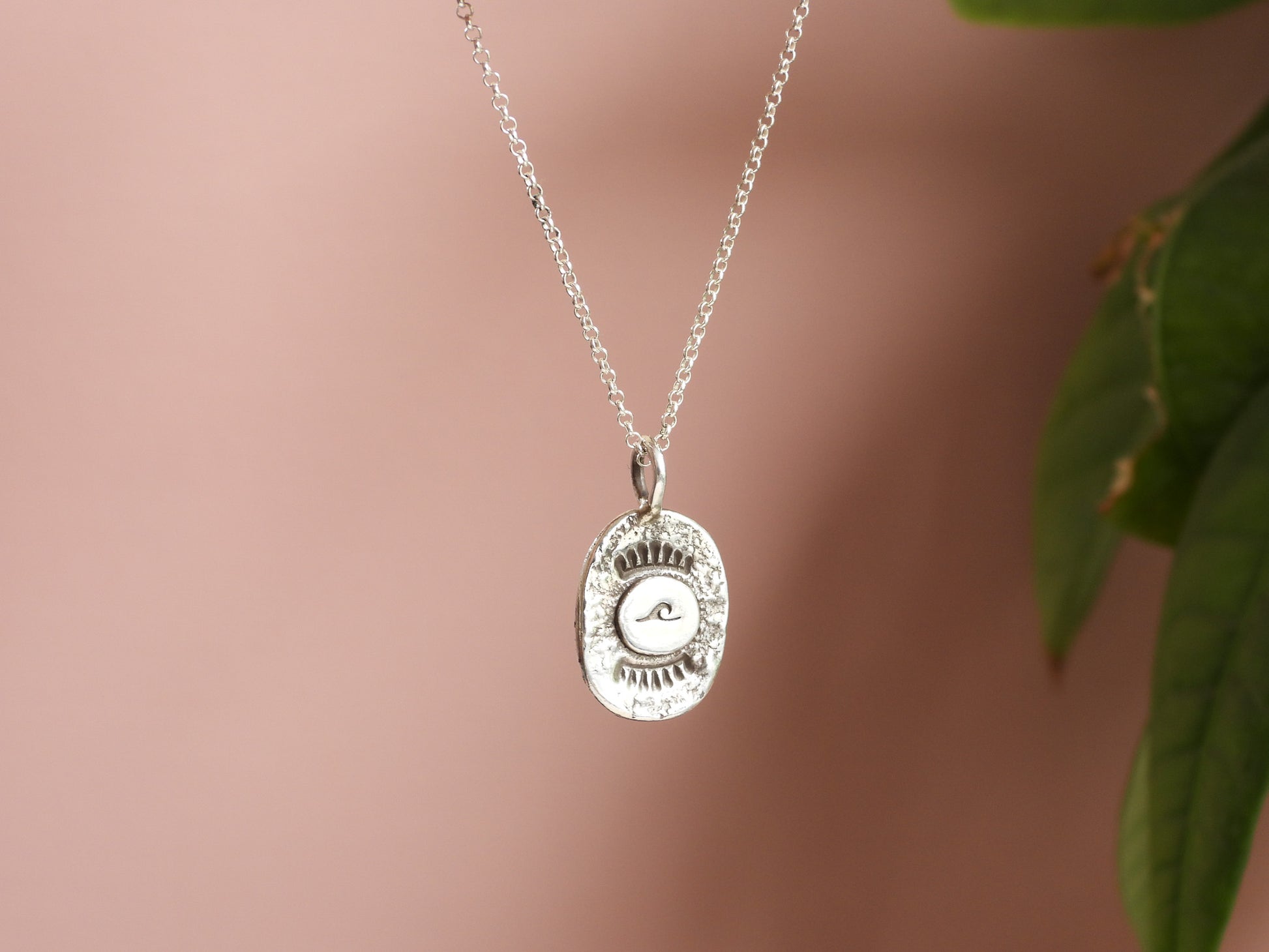 Silver wave necklace with a round pendant on a soft pink background