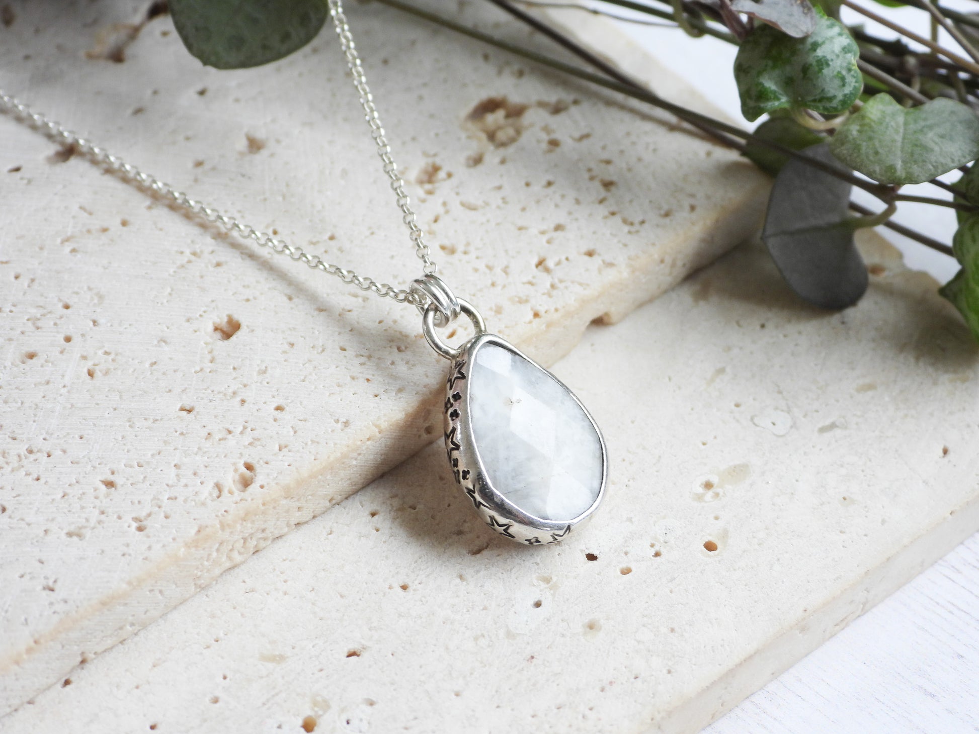 Teardrop-shaped silver moonstone pendant with a white stone on a light stone surface.