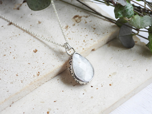 Teardrop-shaped silver moonstone pendant with a white stone on a light stone surface.