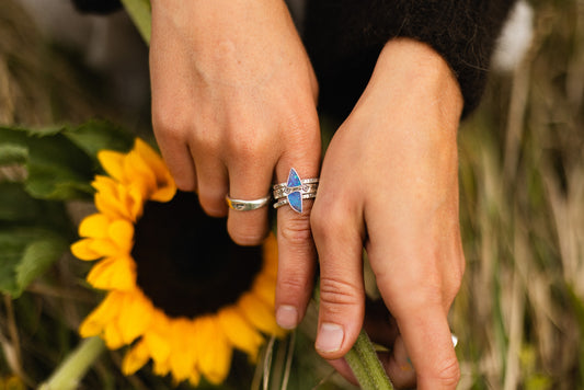 two hands, one wearing a blue Australian boulder opal stacking ring, the other a sunflower