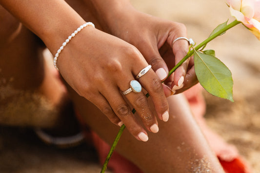 Close-up of hands with larimar rings holding a flower, with a blurred natural background