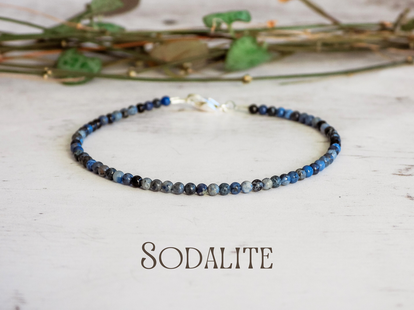 Dainty beaded bracelet with sodalite stones on a light wooden surface with dried plants.