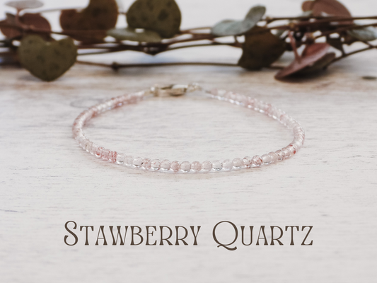 dainty Strawberry quartz bracelet on a light wooden surface with leaves in the background