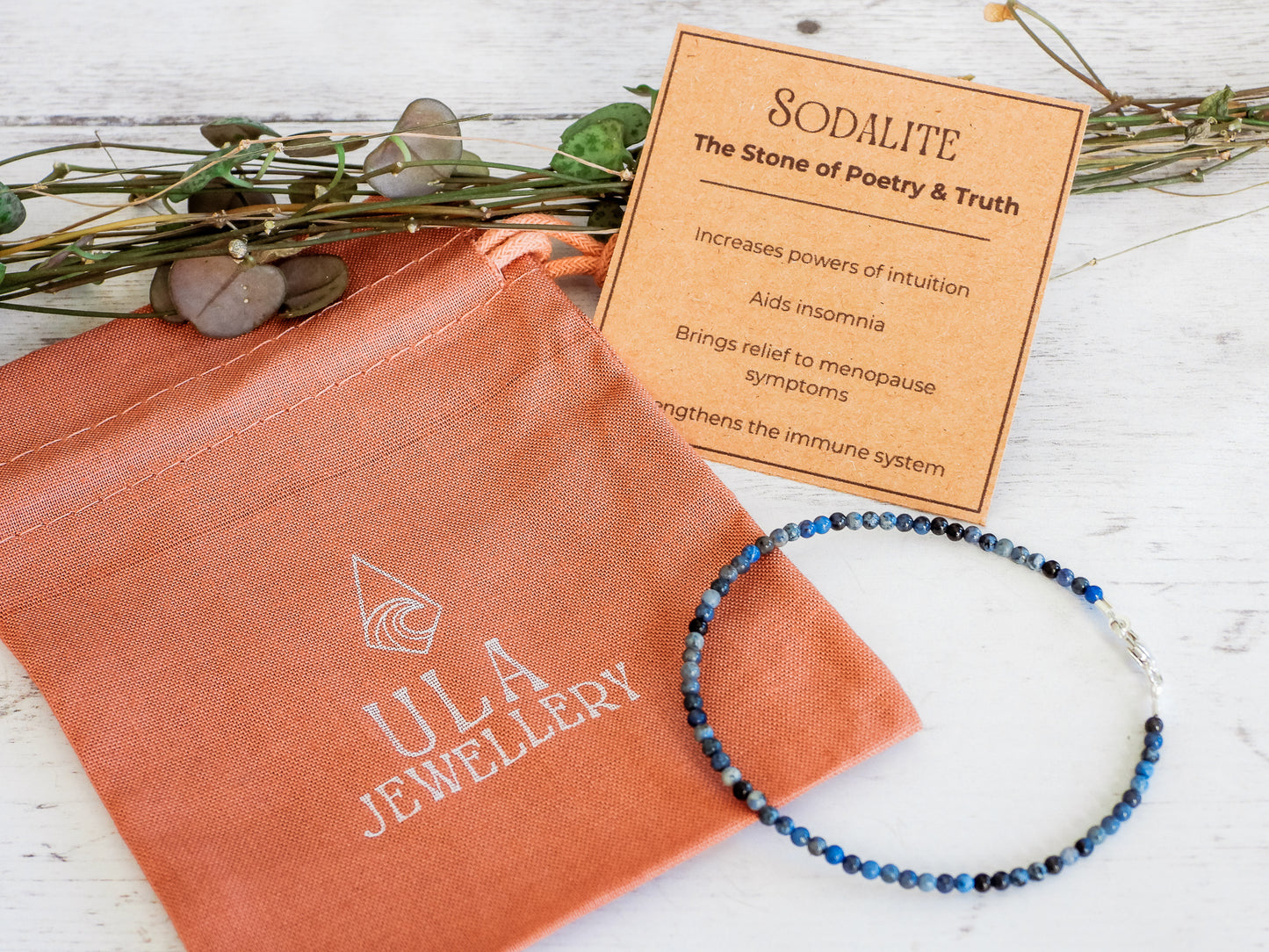 Jewelry set with bracelet and information card on a wooden surface, featuring Ula Jewellery packaging.