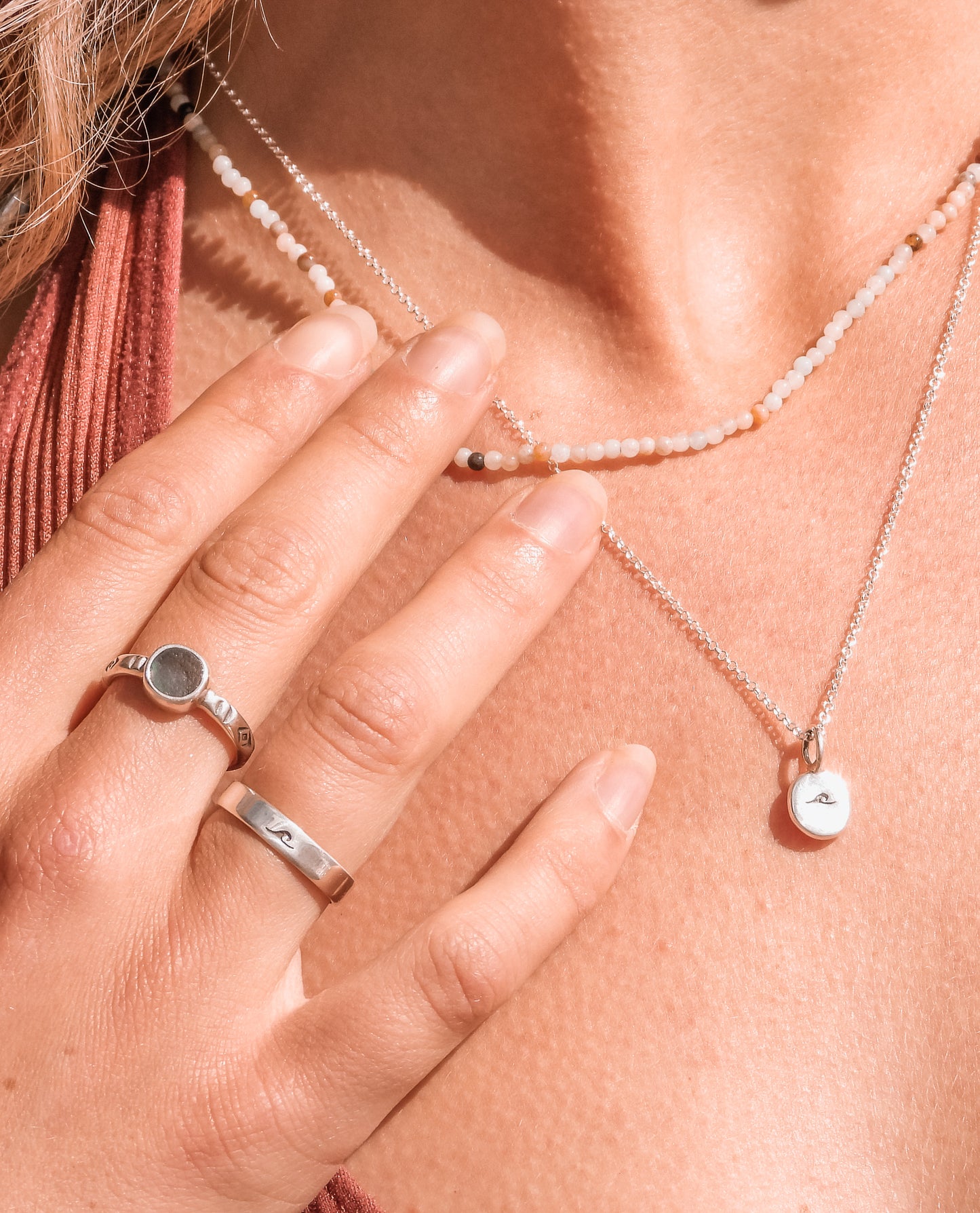 close up of a wave charm necklace and seaglass rings