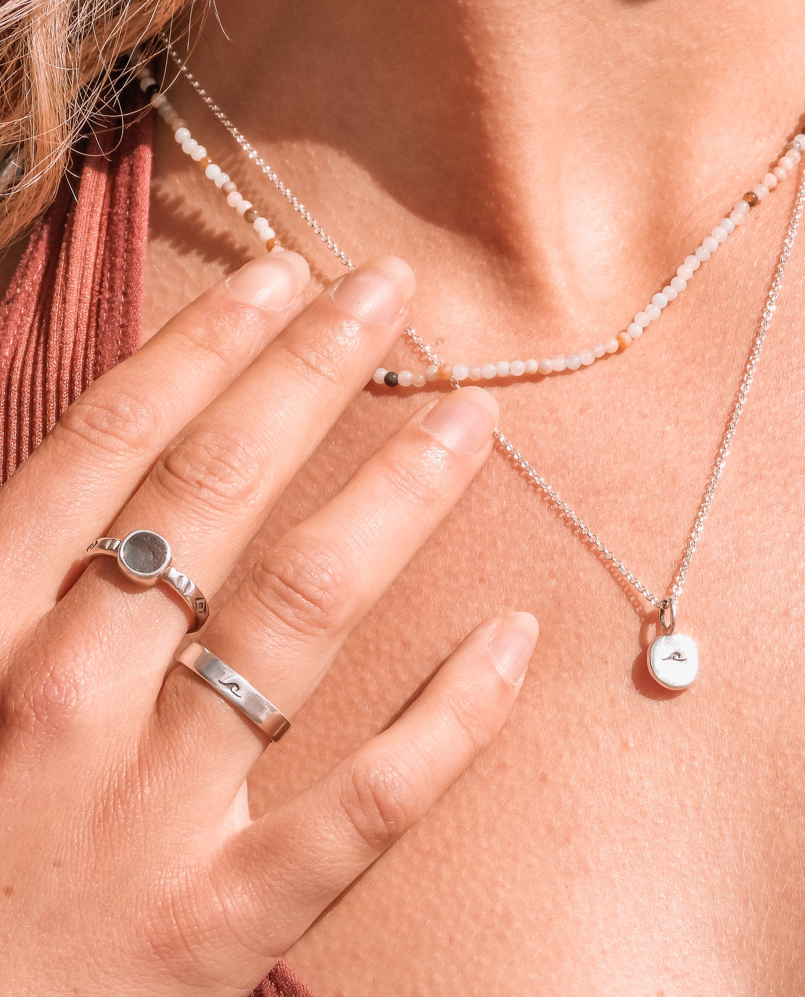 close up of a wave charm necklace and seaglass rings