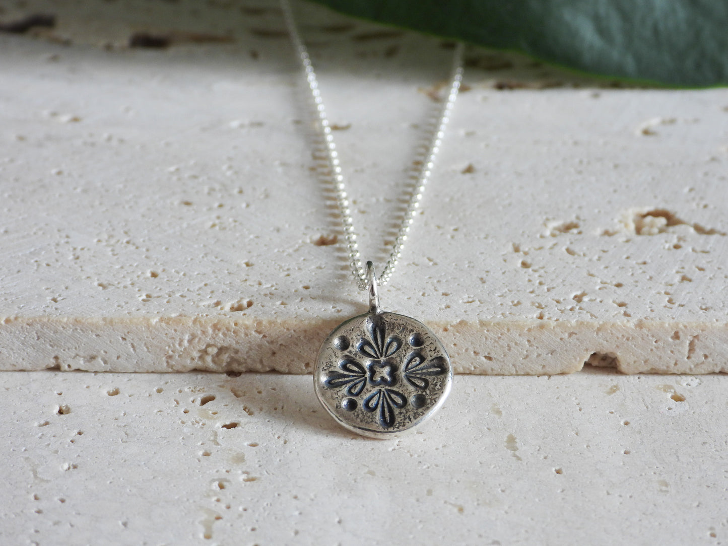 Silver necklace with a detailed pendant on a textured surface