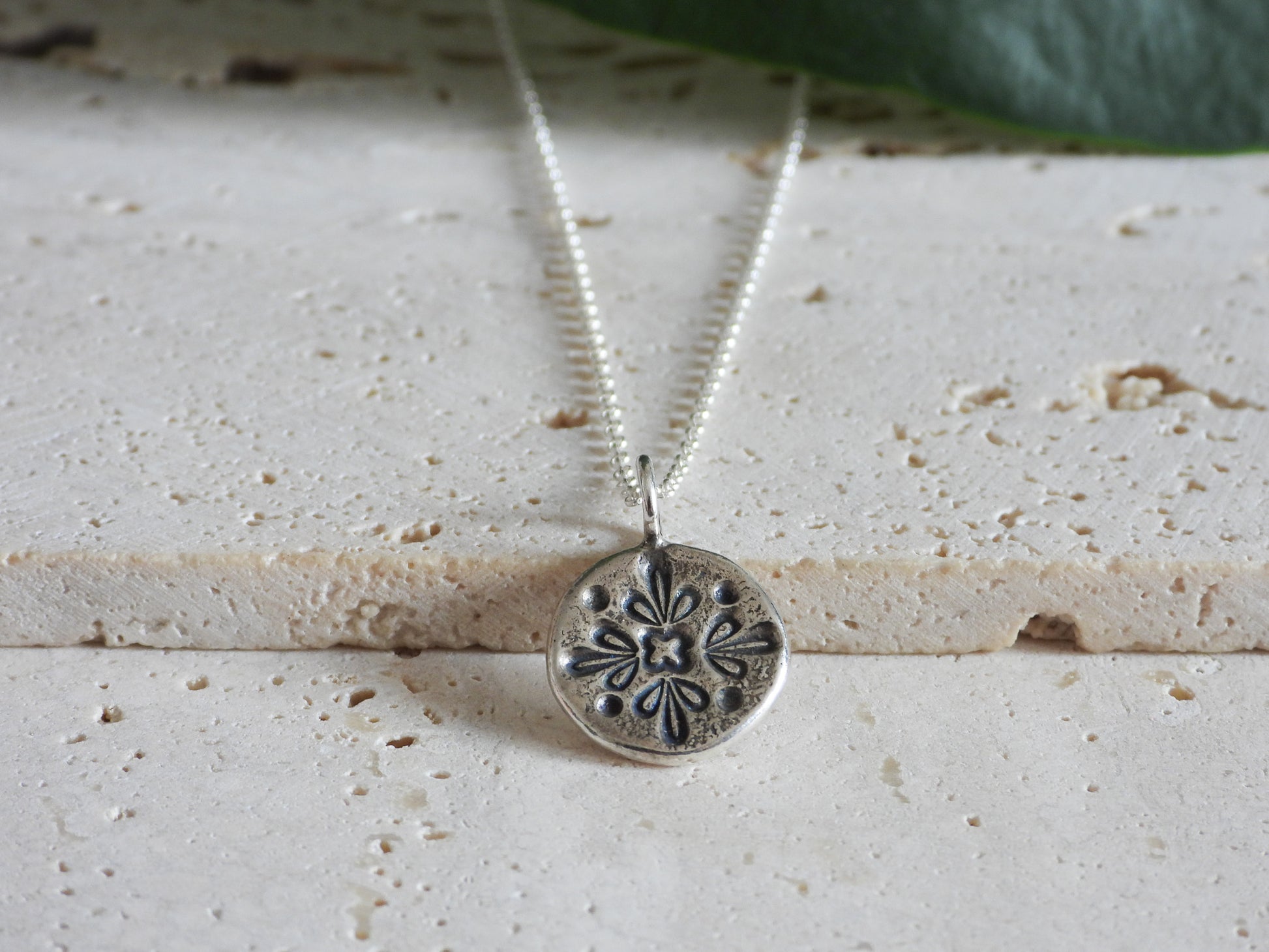 Silver necklace with a detailed pendant on a textured surface