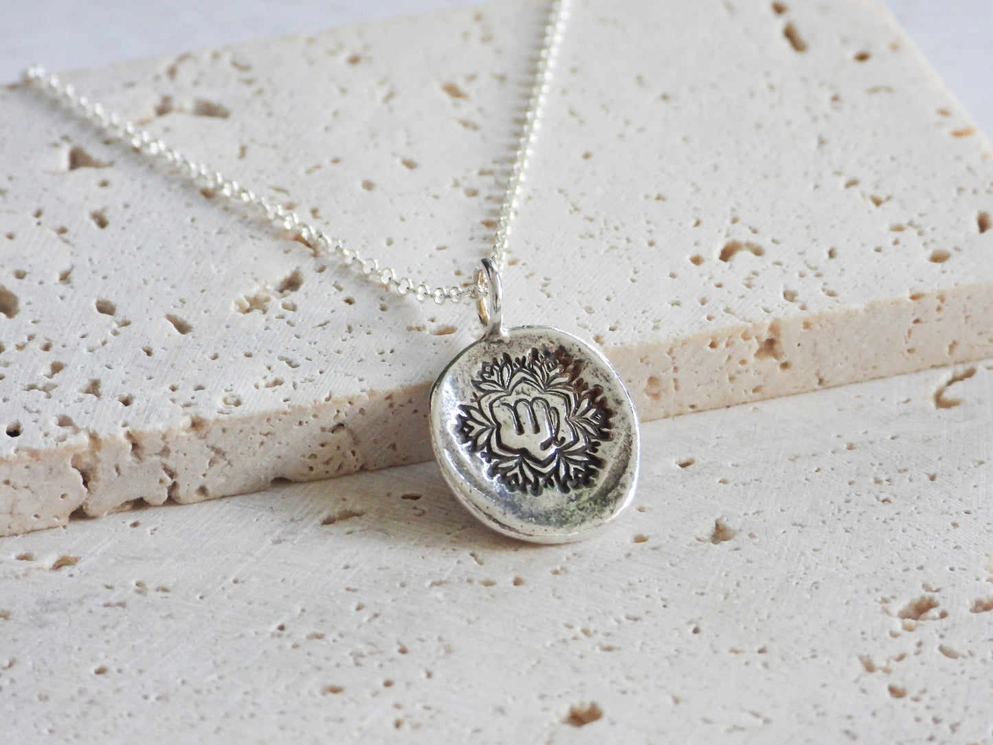 Silver virgo necklace with a round pendant on a textured beige surface