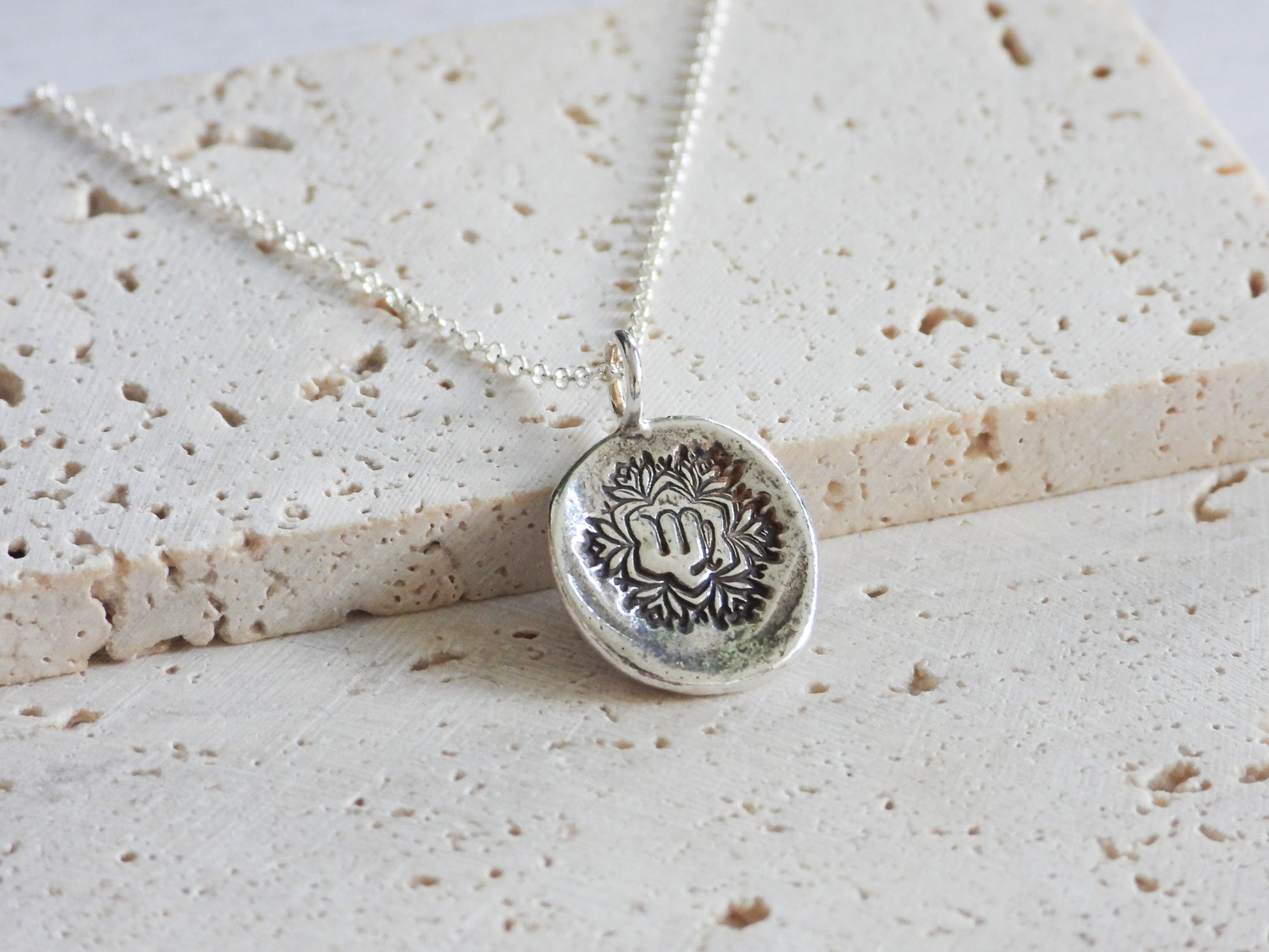 Silver virgo necklace with a round pendant on a textured beige surface