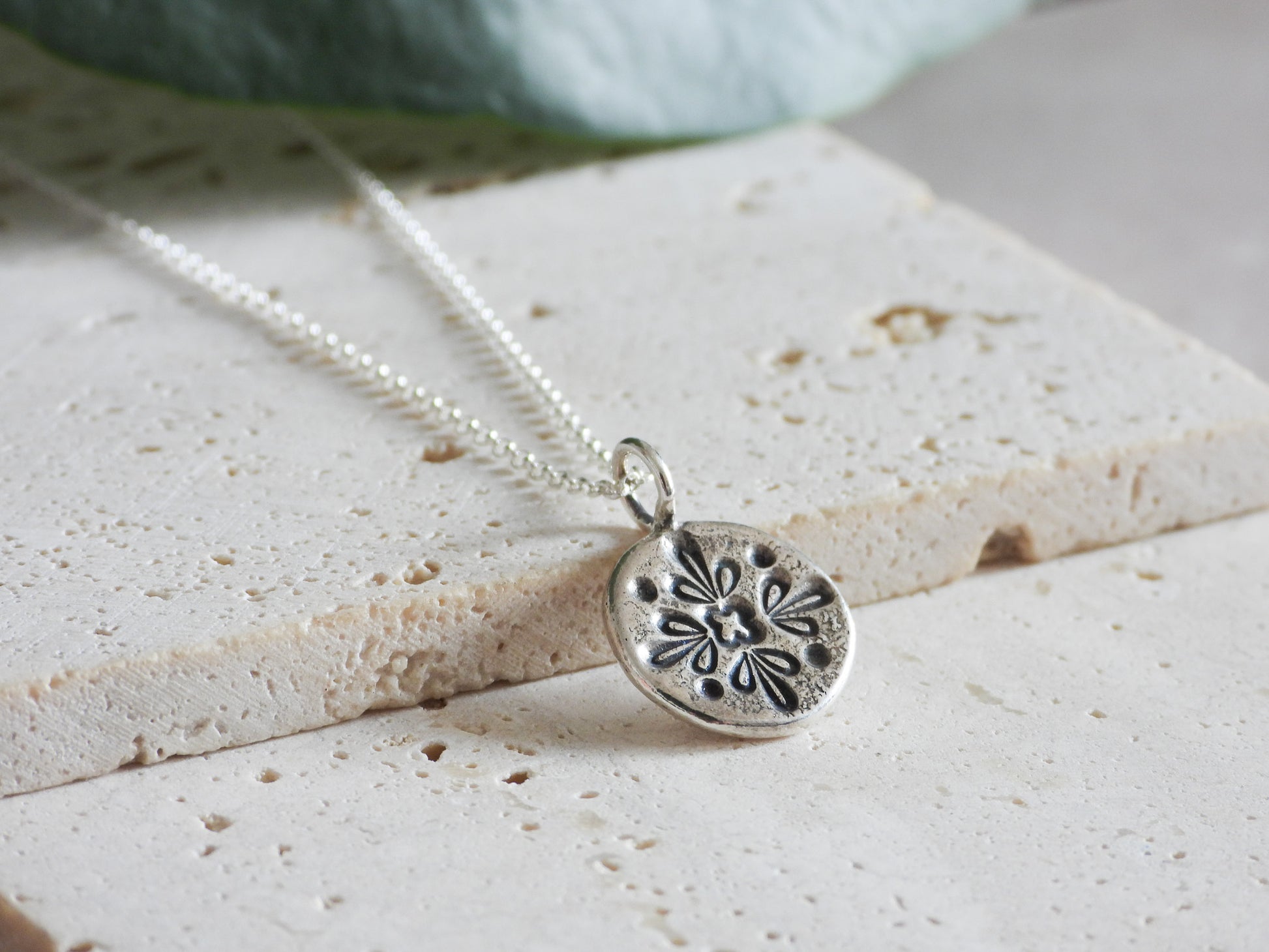 Silver mandala necklace with a detailed pendant on a textured surface