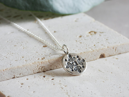 Silver mandala necklace with a detailed pendant on a textured surface