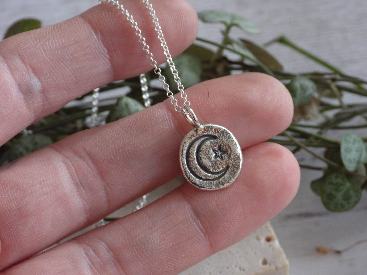 Silver necklace with a moon and star pendant held between fingers against a natural background