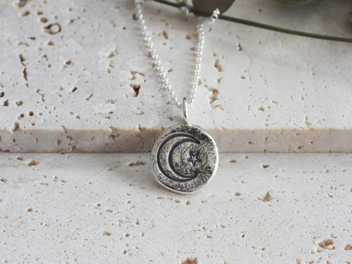 Silver necklace with a circular pendant on a textured surface