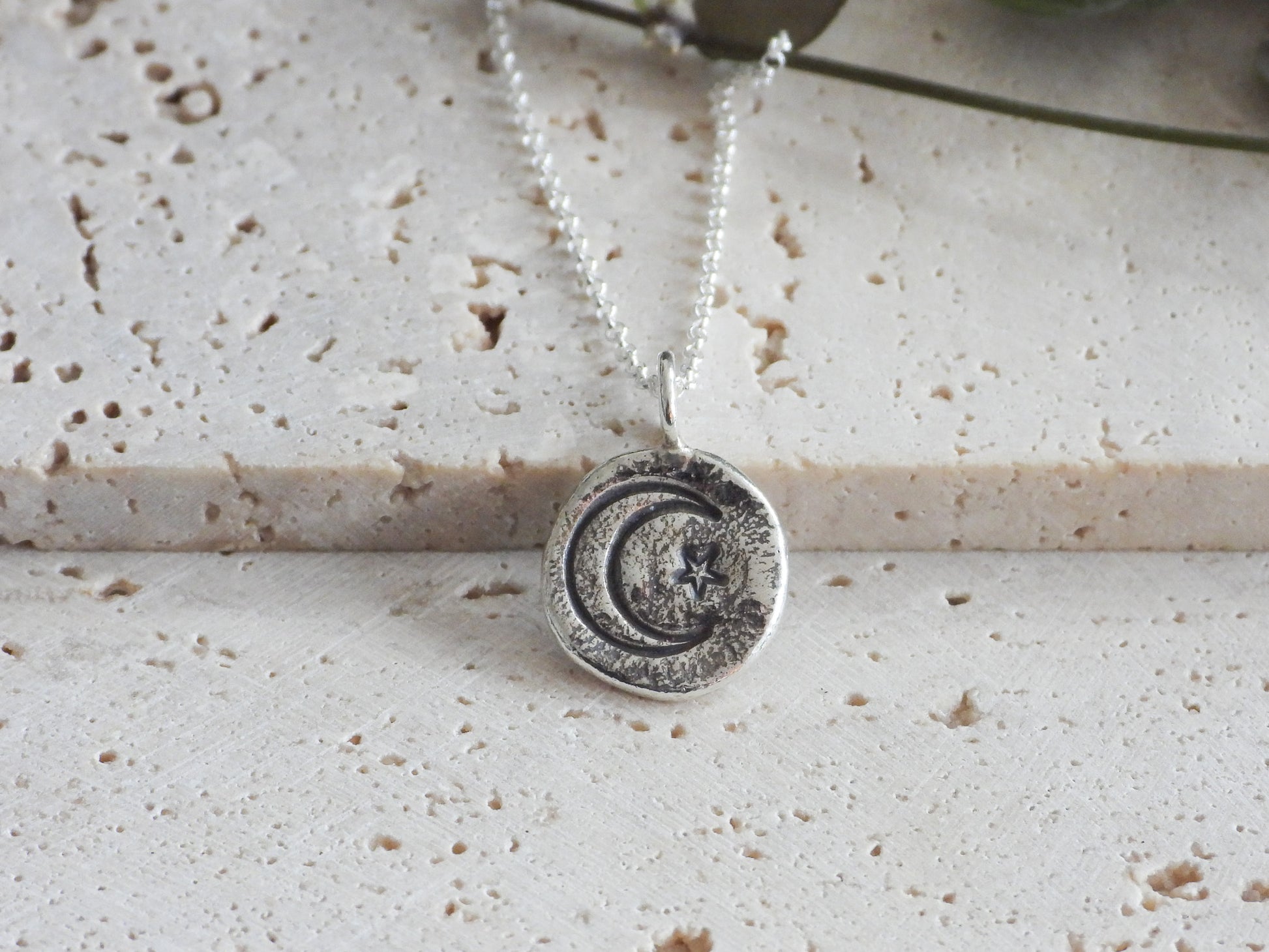 Silver necklace with a circular pendant on a textured surface