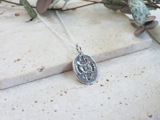 Silver mandala pendant necklace on a light stone surface with greenery