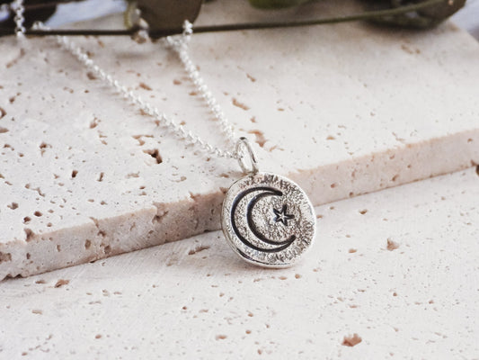 Silver necklace with a moon and star pendant on a textured surface