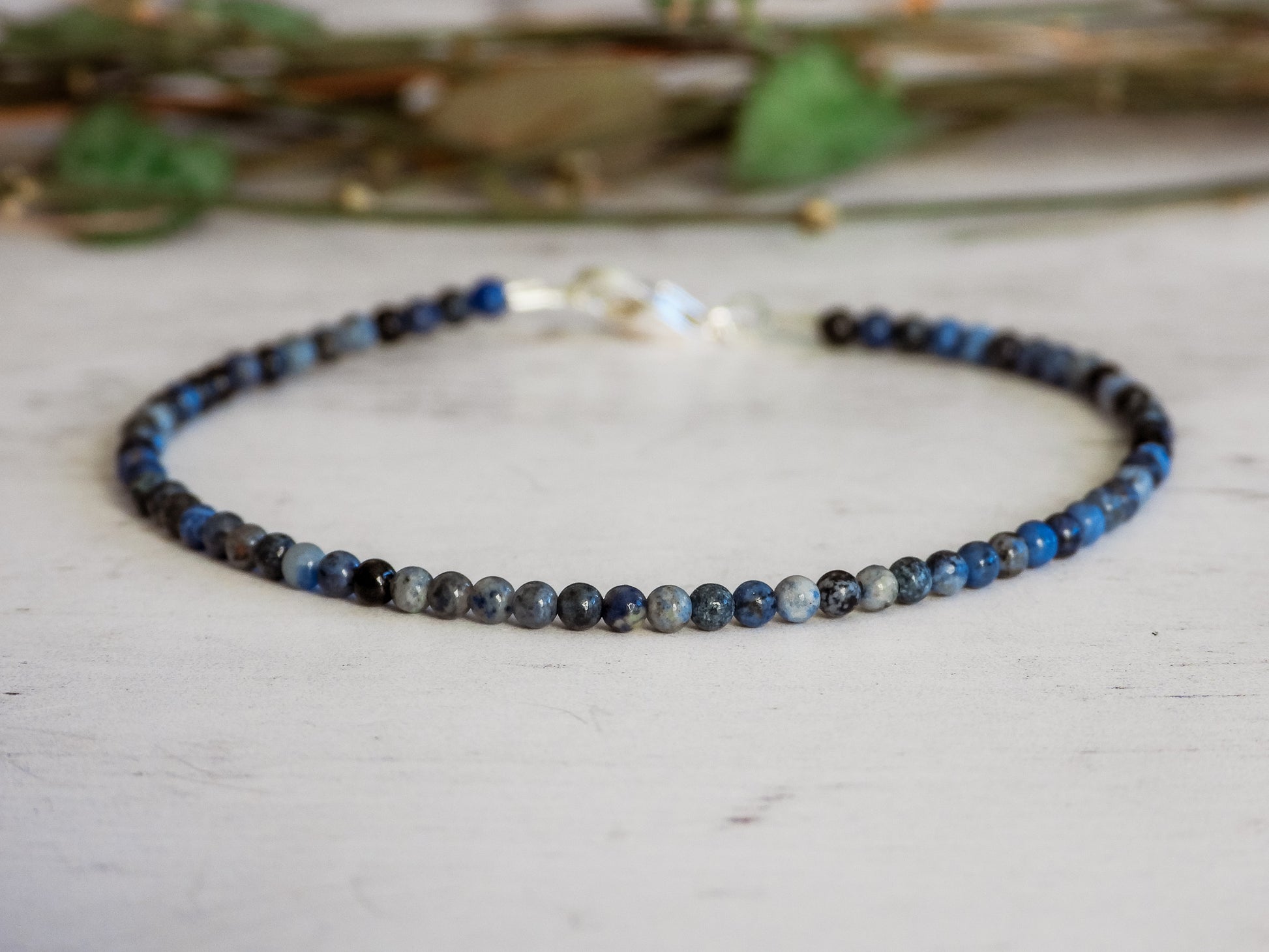 Blue sodalite beaded necklace on a light surface with greenery in the background