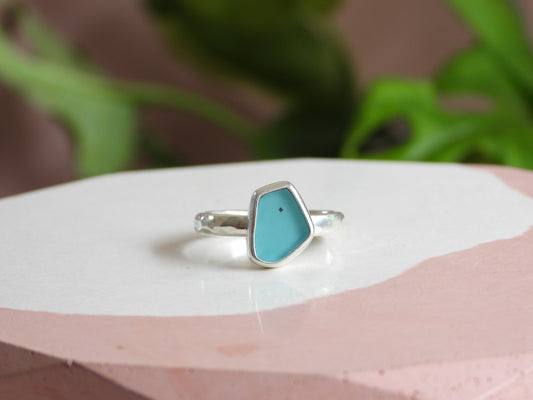 Silver ring with a blue seaglass on a white surface with greenery in the background